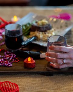 a hand holding a glass of wine at a dinner table with a Valentine's day setting