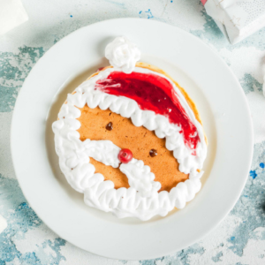 Pancake with whipped cream and cherry to look like Santa Claus