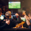 three men raising their glasses while watching football