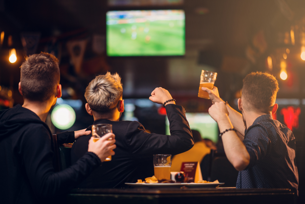 three men raising their glasses while watching football