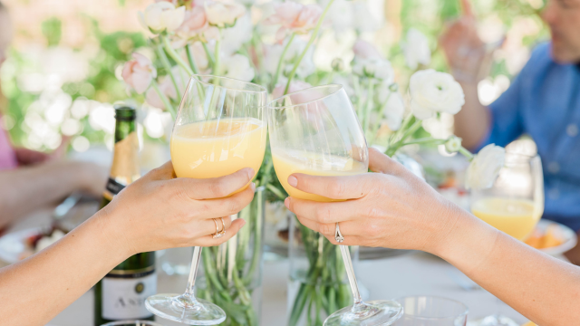 Two people clinking glasses of mimosa